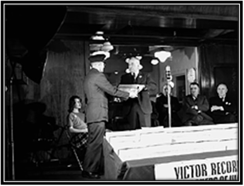 L'honorable Major-général L.R. LaFlèche, ministre des Services nationaux de guerre, reçoit des mains de F.R. Deakins, président de RCA Victor, des disques destinés aux prisonniers de guerre canadiens détenus dans les camps de détention allemands.