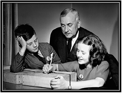 L'honorable Major-général L.R. LaFlèche, ministre des Services nationaux de guerre, regarde sa fille adresser un colis contenant des disques de phonographe sous les yeux de son fils lors d'une visite à l'usine R.C.A. Victor.